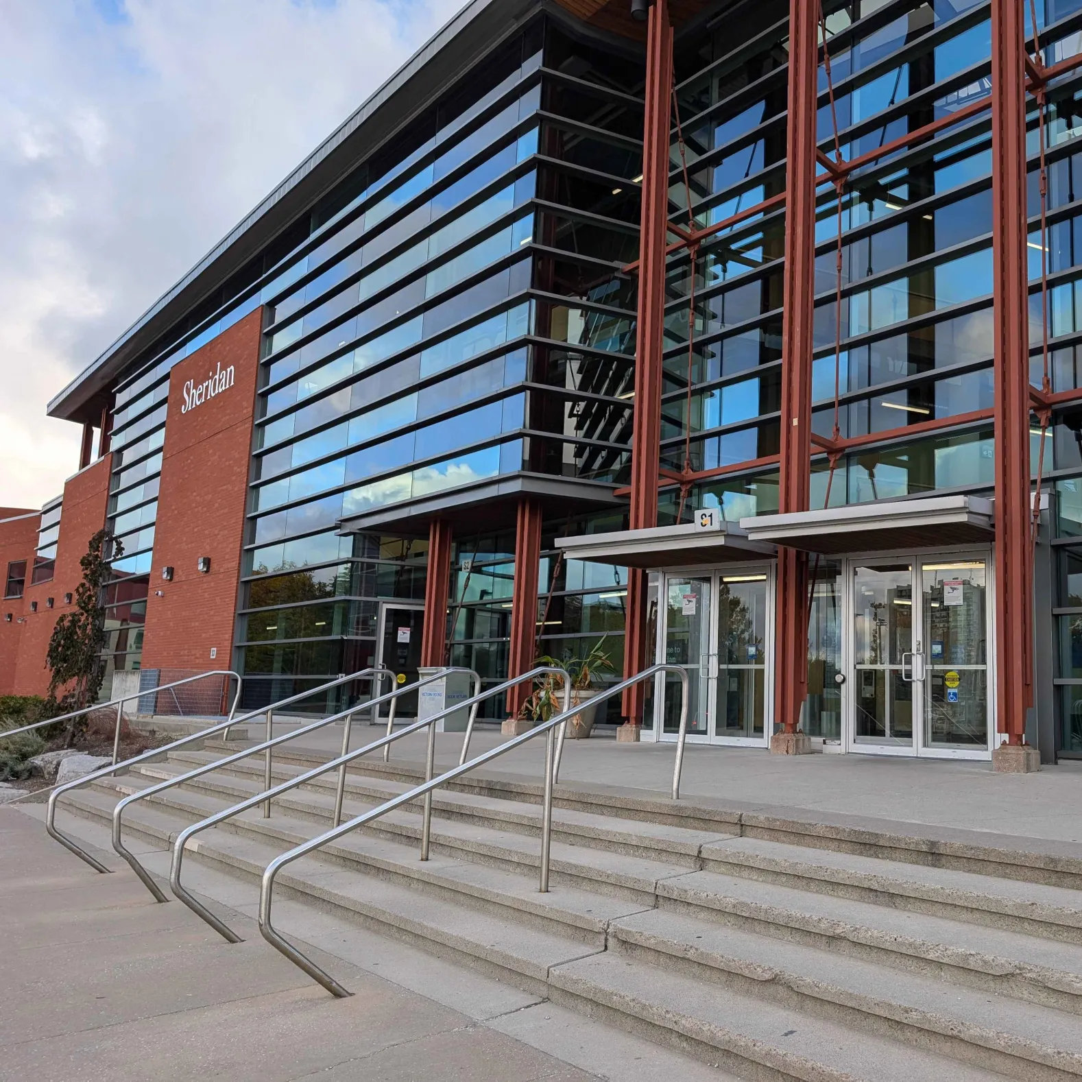 SCAET building of Sheridan College Trafalgar Campus. <br> The materials of this building involve 
                metal, colored glass, and bricks atop concrete. The space is modern and simplistic and its
                open area allows students to socialize or navigate around campus.